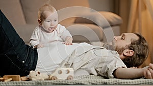 Caucasian family father with little daughter son lie on floor at home play. Baby girl boy newborn kid crawling over