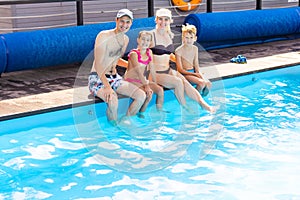 Caucasian family having fun by their swimming pool. Happy young family splashing water with hands and legs while sitting