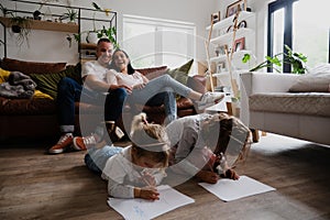 Caucasian family in the living room together, spending quality family time. Kids drawing on the floor while mother and