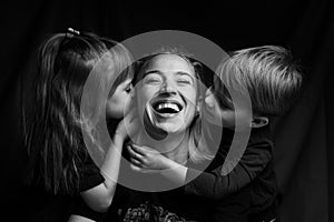 Caucasian Family Portrait in Black and White. mom daughter and son. mom laugh. son and daughter kiss mom on the cheeks