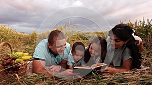 A caucasian family is reading a book on a picnic in a wheat field in slow motion