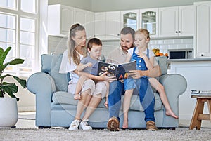 Caucasian family reading a book together on the couch at home. Mother and father teaching their little son and daughter