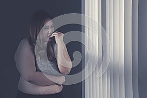 Caucasian fat woman looks sad near the window