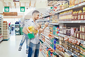 Caucasian father dad in grocery store shopping buying food and holding carrying baby son under arm. Man parent with toddler kid