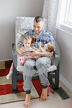 Caucasian father dad sitting with toddler daughter and newborn infant son watching cartoons on smartphone.