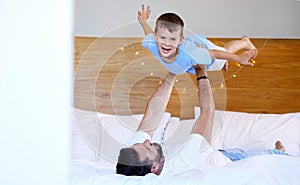 Caucasian father lifting his cute little son in the air to pretend to fly like a plane or superhero with arms out on a