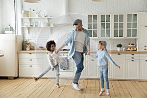 Caucasian father multiethnic daughters dancing in modern cozy kitchen