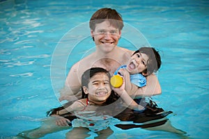 Caucasian father in pool with biracial children, holding disabled son