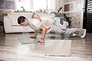 Caucasian father and small daughter in casual clothes do pushup pressup exercise on carpet on warm floor in living room, sporty