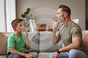 Caucasian father and son communicating using sign language while sitting on the couch at home