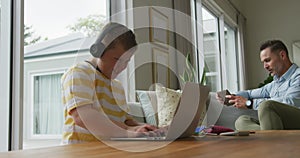 Caucasian father with son sitting in living room, using laptop and smartphone