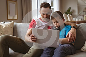 Caucasian father and son using laptop sitting on the couch at home