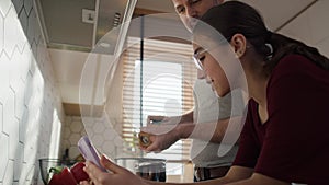 Caucasian father with teenage daughter looking at mobile phone in kitchen while cooking.