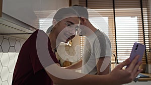 Caucasian father with teenage daughter looking at mobile phone in kitchen while cooking.