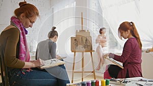 Caucasian female artists performing artistic etude witn naked model in drawing studio