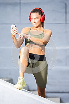 Caucasian Female Athlet In Running Outfit During Her Stretching Exercises Outdoor. Listening Music in Headphones