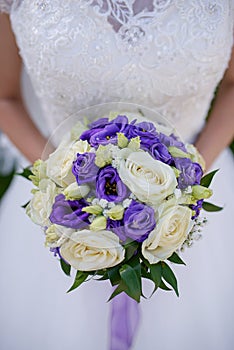 Caucasian female in beautiful lacy white dress holding a large round bouquet featuring ivory and purple roses