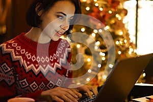 Caucasian female blogger in red winter sweater texting and reading connected to 4g wireless in xmass interior