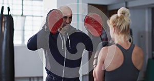 Caucasian female boxer wearing boxing gloves training her punches with male trainer at the gym