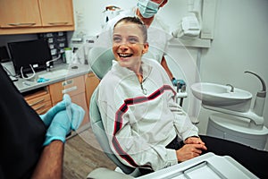 Caucasian female client smiling while sitting on dentist bed chatting to doctors after surgical procedure