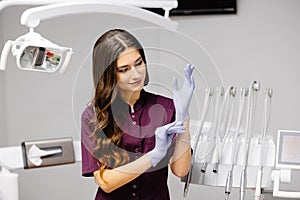 Caucasian female dentist putting on blue sterilized surgical gloves in the medical clinic