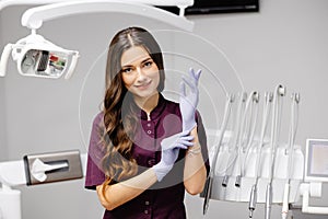 Caucasian female dentist putting on blue sterilized surgical gloves in the medical clinic