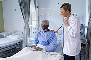 Caucasian female doctor examining with stethoscope african american male patient in hospital room