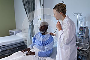 Caucasian female doctor examining with stethoscope african american male patient in hospital room