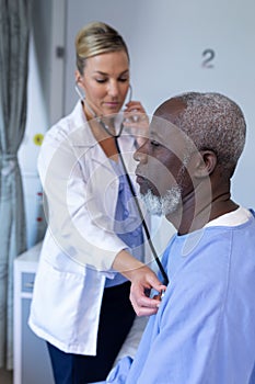 Caucasian female doctor examining with stethoscope african american male patient in hospital room