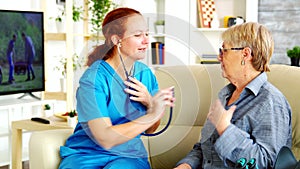 Caucasian female doctor in nursing home listening old woman heartbeat