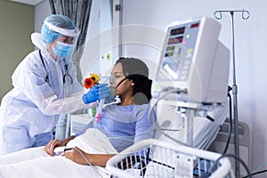 Caucasian female doctor in ppe suit checking african american female patient with ventilator photo