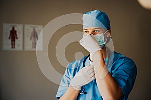 Caucasian female doctor or surgeon in scrubs preparing for surgery, medical gloves and mask