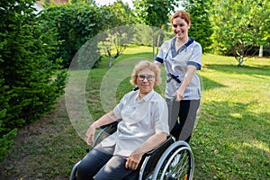 Caucasian female doctor walks with an elderly patient in a wheelchair in the park. Nurse accompanies an old woman on a