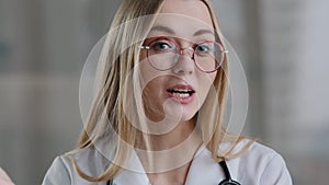 Caucasian female doctor wear eyeglasses make online video call in hospital clinic consult patient remote distant