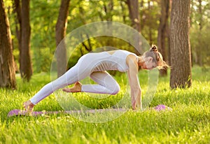 Caucasian female doing yoga on green grass in summer on nature.