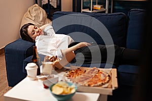 Caucasian female falling asleep after eating junk-food in living room late at night