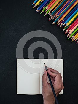 Caucasian female hand writing on notebook, colorful pencils background