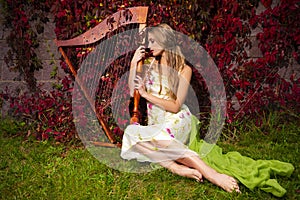 caucasian female harpist posing with harp against ivy wall outdoor