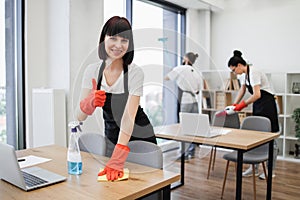 Caucasian female janitor in black apron cleaning table with detergent