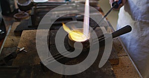 Caucasian female jeweller in workshop wearing apron, using gas burner, melting metal