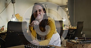 Caucasian female jeweller in workshop wearing apron, using tablet, smiling at camera