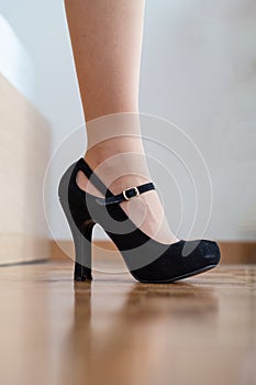 Caucasian female legs close up shot wearing black high heel shoes inside on wooden tile pavement