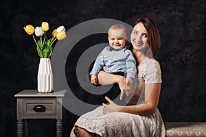 Caucasian female parent and son baby boy sitting together on couch indoors. Happy mother day holiday