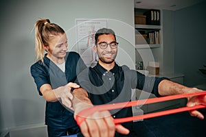 Caucasian female physiotherapist assisting male patient holding resistance band