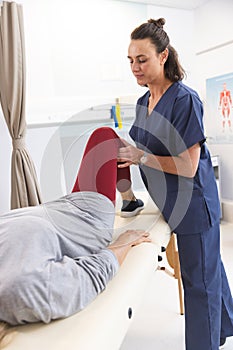 Caucasian female physiotherapist and senior woman stretching leg at hospital