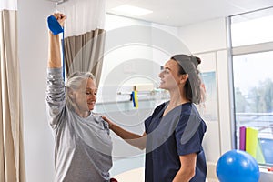 Caucasian female physiotherapist and senior woman using exercise band stretching arms