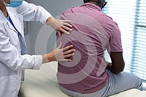 Caucasian female physiotherapist wearing mask palpating back of african american male patient