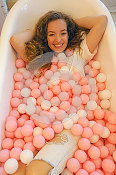 Caucasian female pretty model funny posing in bath tube with color ball