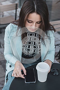 Caucasian female searching something on her phone while drinking a coffee