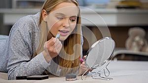 Caucasian female student trying on gloss lipstick near mirror, face beautifying